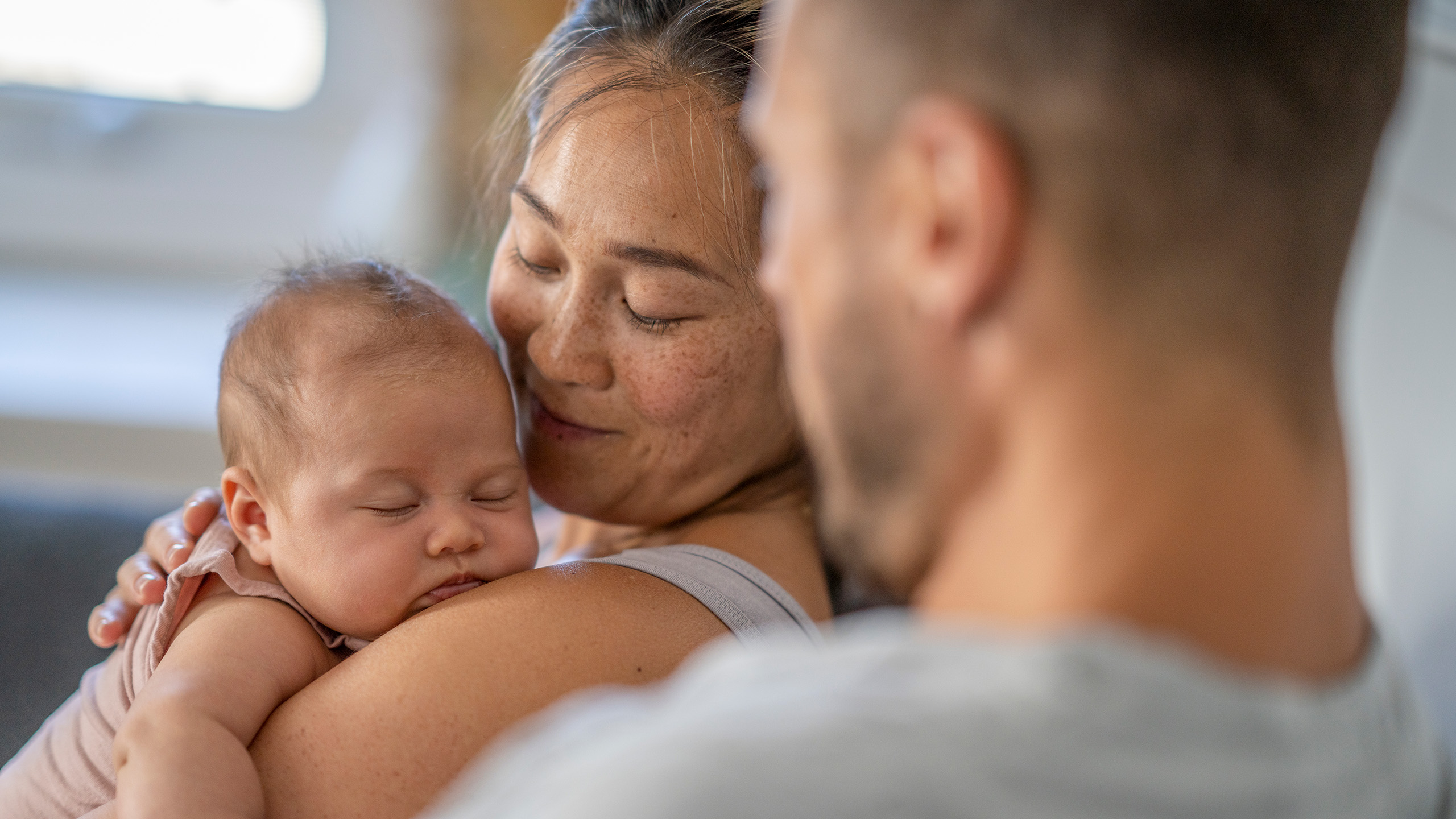 A mother lovingly holding her newborn baby, with father looking at them both.